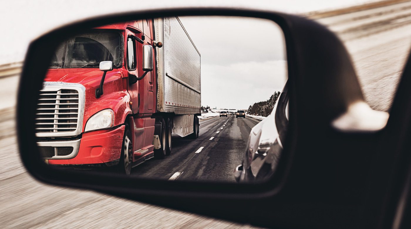 Semi-truck-in-the-rear-view-mirror-of-a-passenger-vehicle