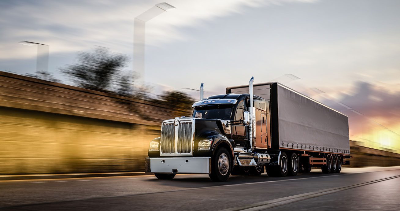 Black-semi-truck-driving-fast-on-highway-at-sunset