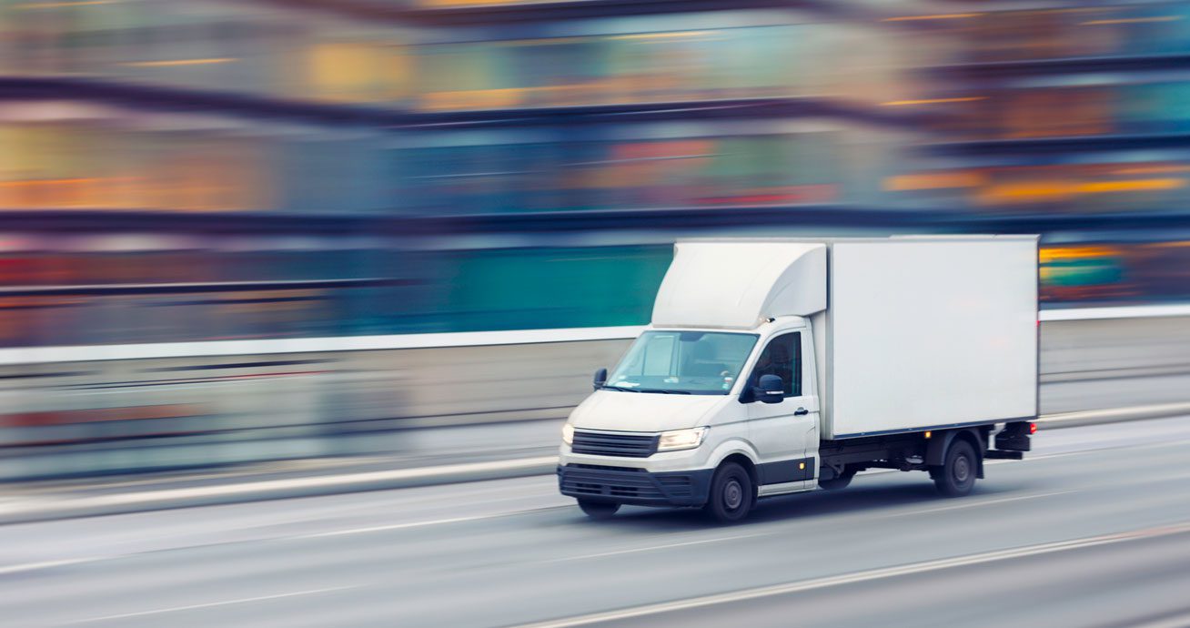 Delivery-truck-driving-through-city-street-between-buildings