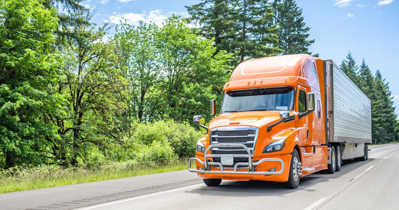 Orange-semi-truck-driving-on-road-with-trees-in-background