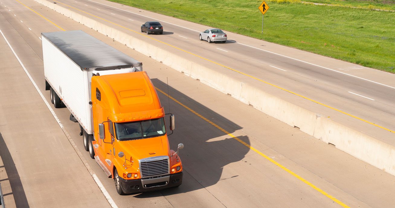 Orange-semi-truck-traveling-on-divided-highway-with-passing-cars