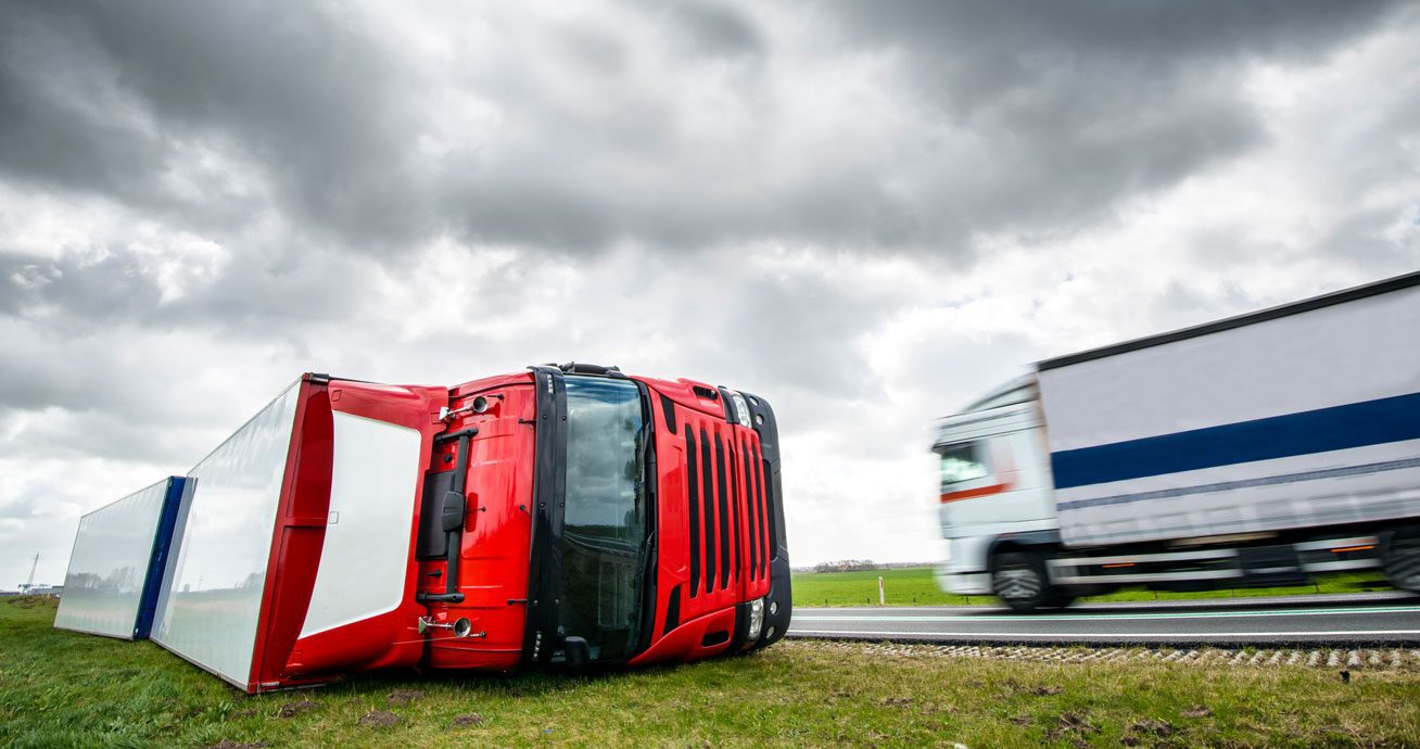 Overturned-red-truck-on-roadside-with-passing-vehicle