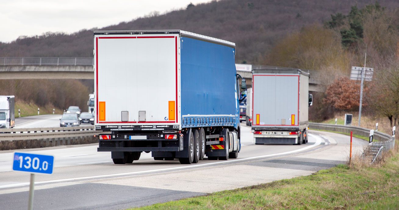 Two-box-trucks-driving-on-highway-near-overpass-with-surrounding-traffic