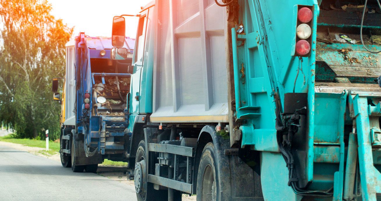 Two-garbage-trucks-parked-along-roadside-in-a-line