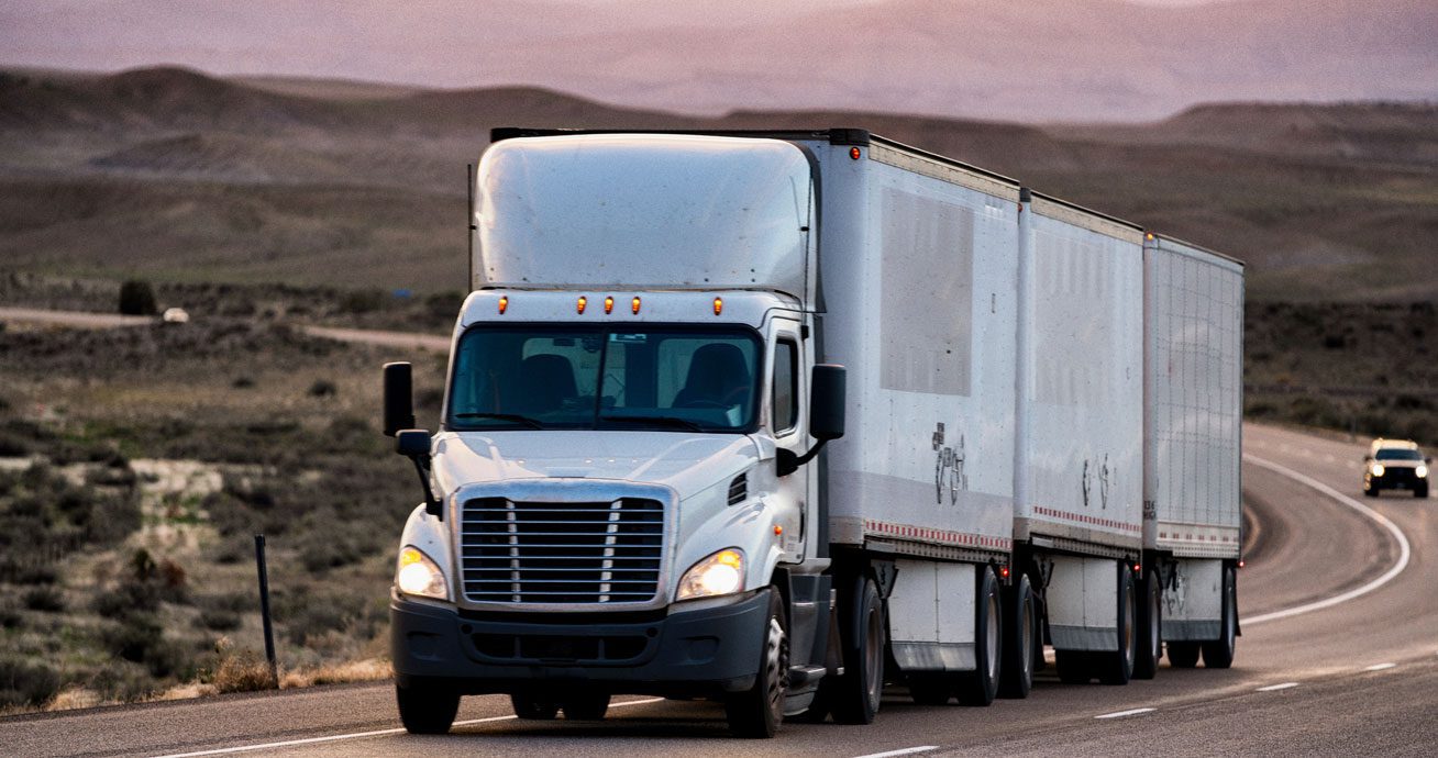 White-semi-truck-driving-on-desert-highway-with-mountains-in-background