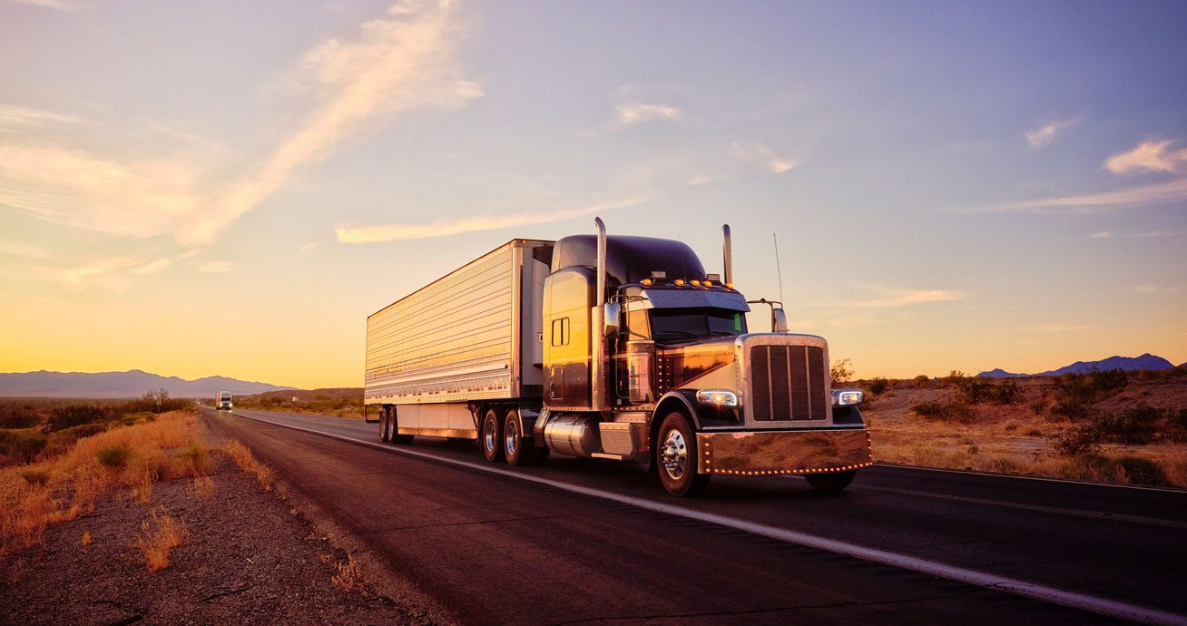 White-semi-truck-driving-on-open-highway-with-mountains-in-distance