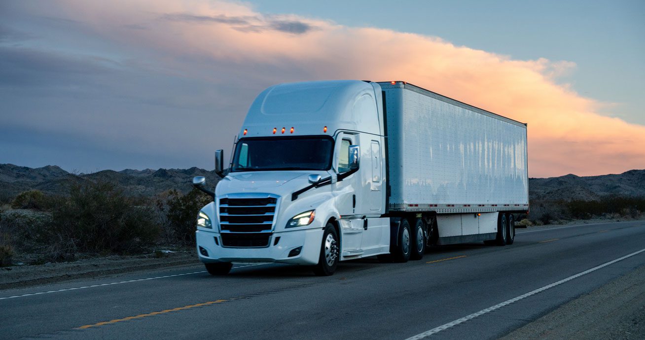 White-semi-truck-driving-on-road-at-sunset