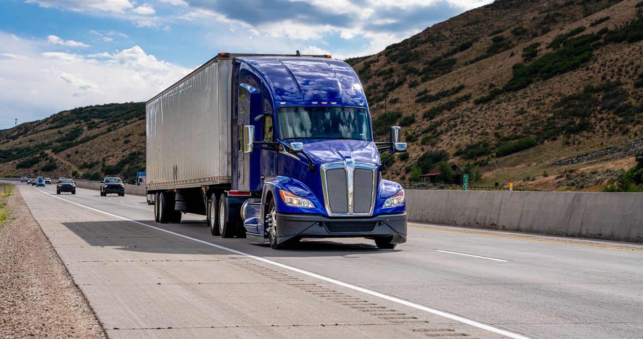 Blue-semi-truck-driving-on-highway-with-hills-in-background