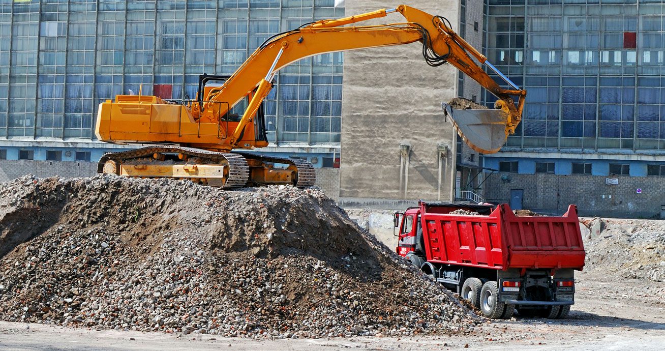 Excavator-loading-dirt-into-red-dump-truck-at-construction-site