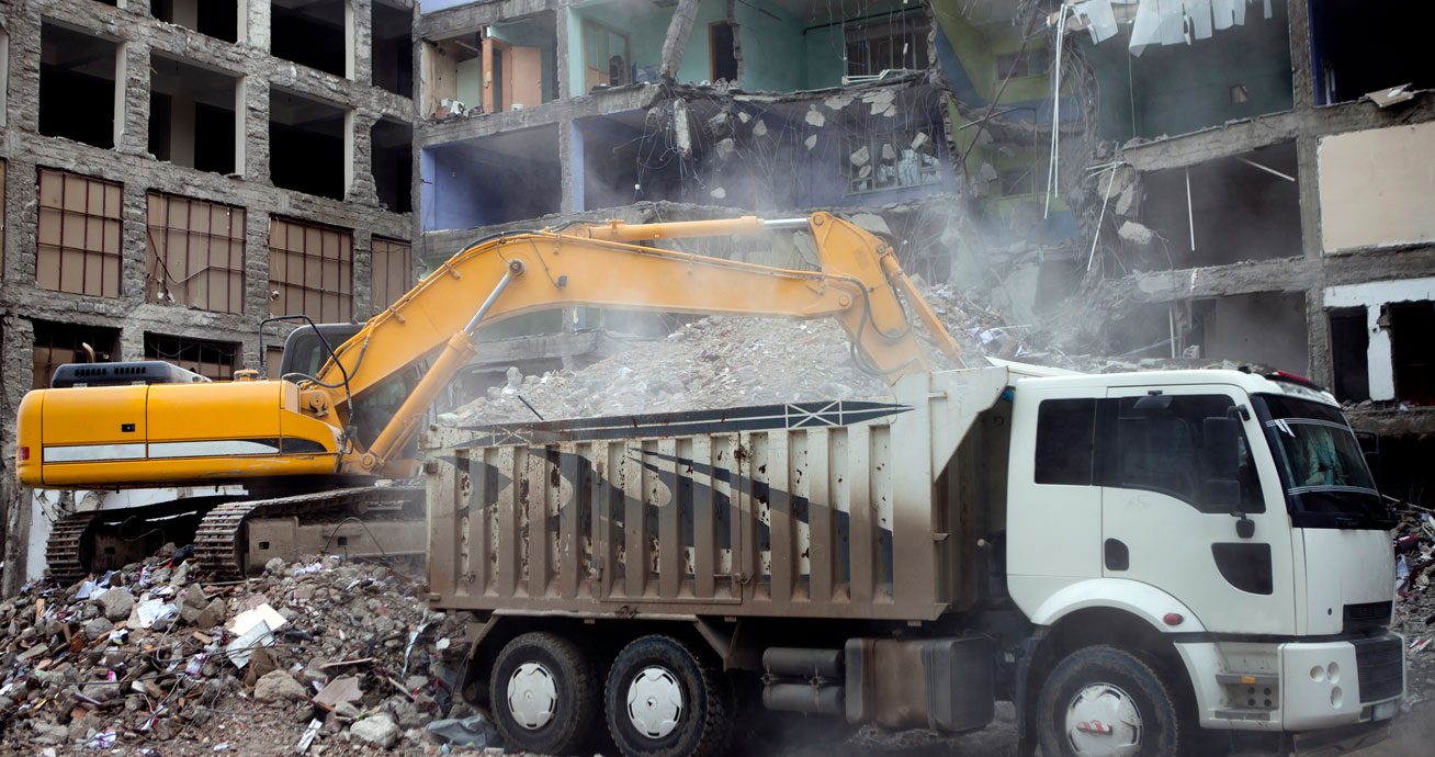 Excavator-loading-soil-into-dump-truck-beside-building