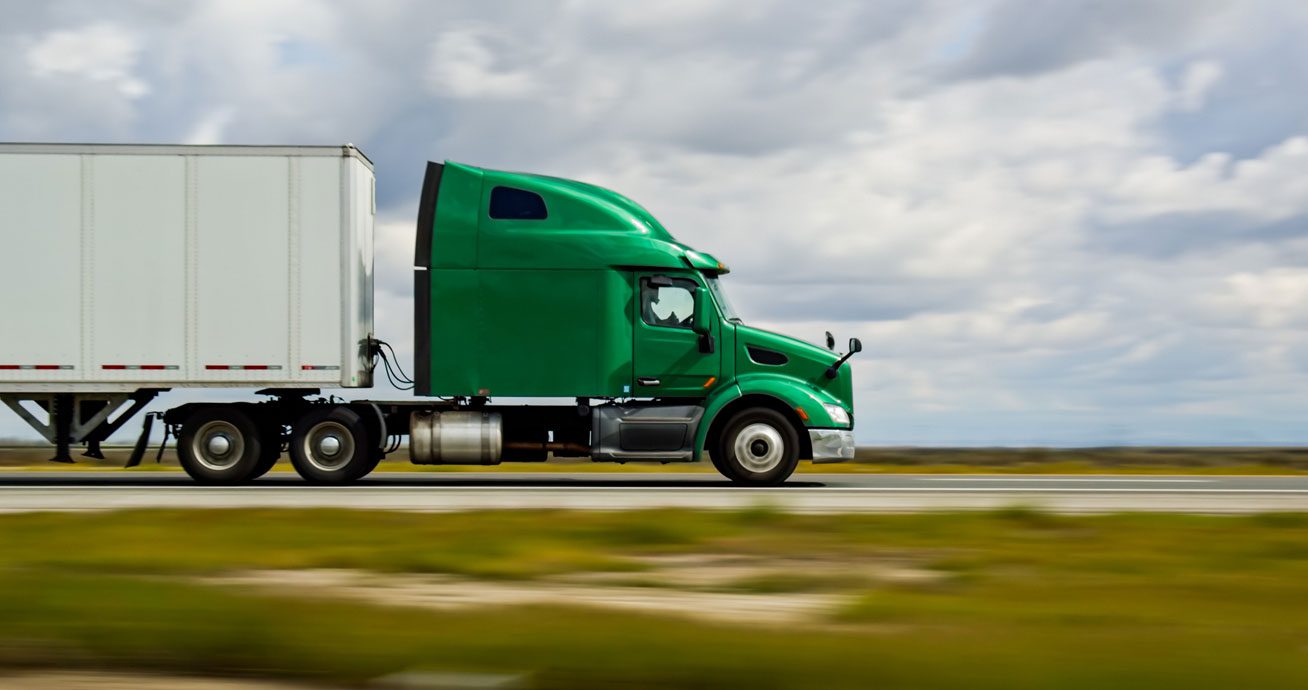 Green-semi-truck-pulling-trailer-driving-along-highway