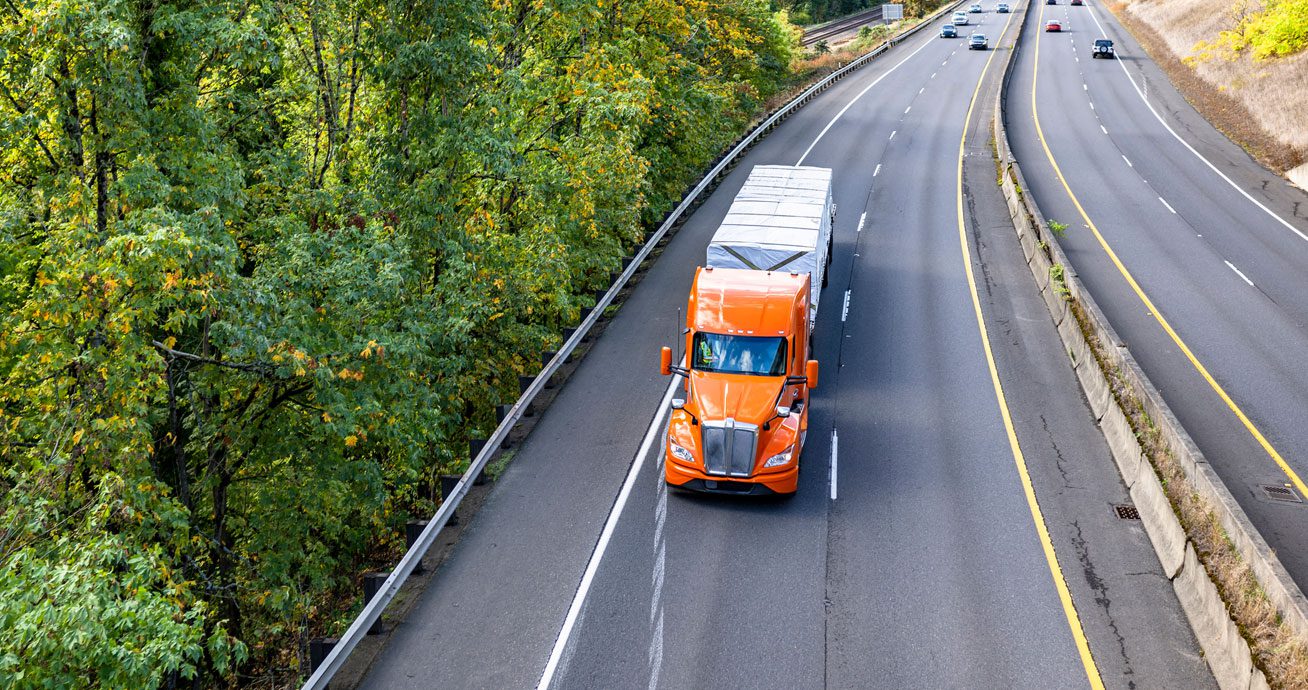 Orange-semi-truck-driving-on-highway-next-to-tree-line