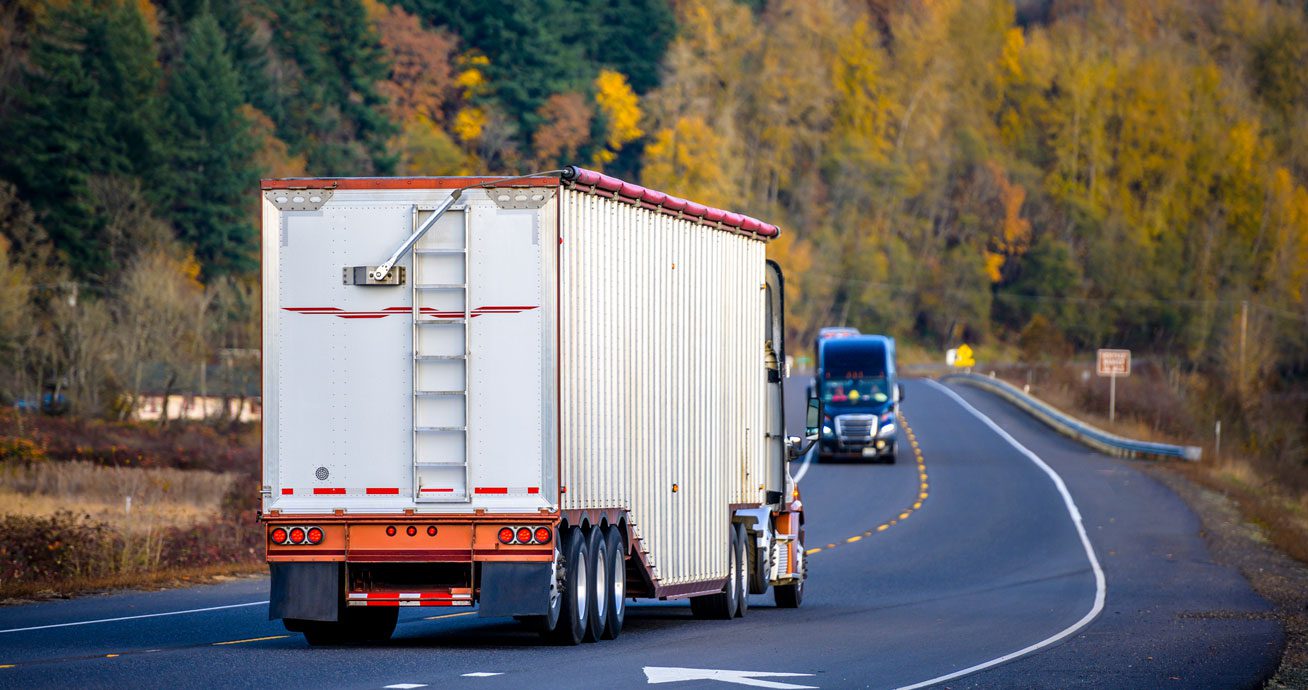 Rear-view-of-trailer-truck-driving-on-curved-road-through-trees