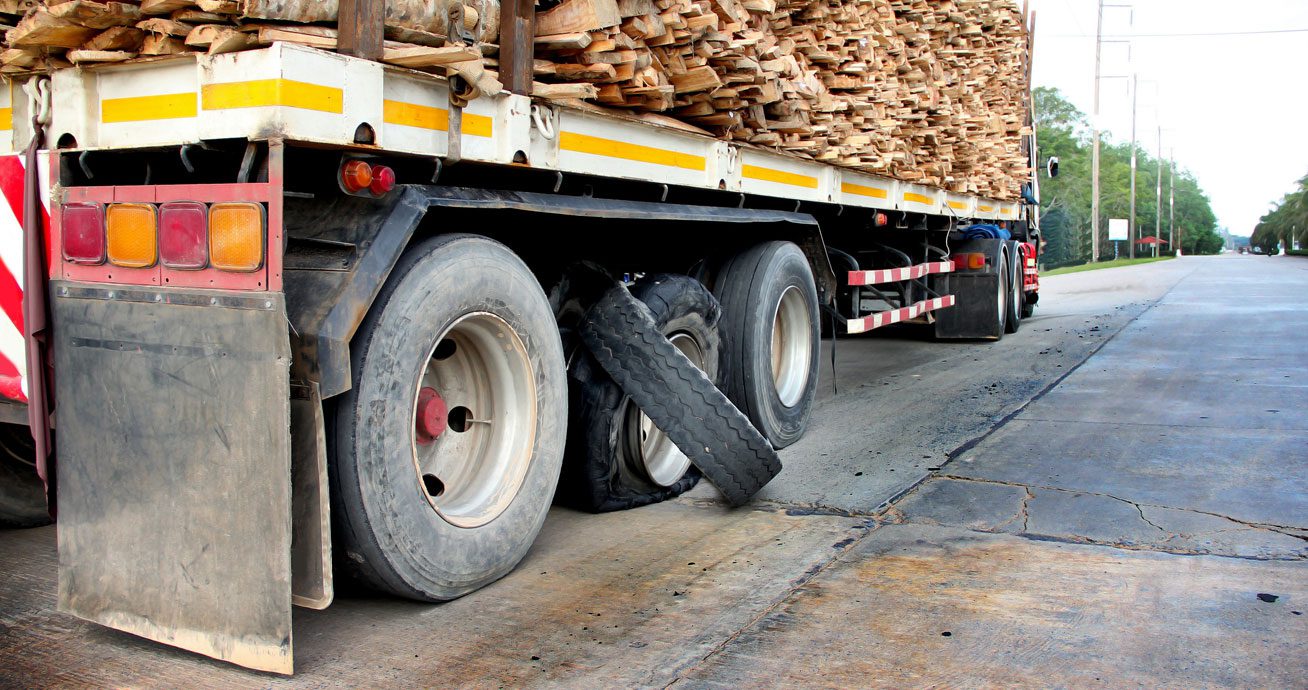 Truck-trailer-loaded-with-wood-and-damaged-rear-tire-on-roadside