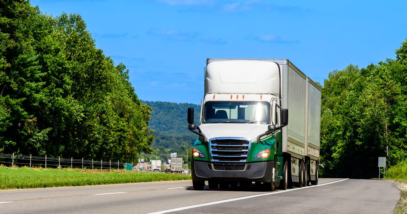 White-semi-truck-driving-on-road-between-trees